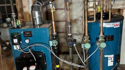 Basement boiler and indirect water tank joined by copper manifold piping and circulator pumps