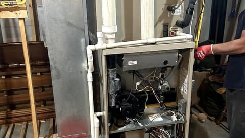Furnace with the front panel removed showing the burner compartment and wiring, an orange bucket on the basement floor